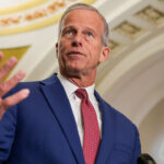 Low angle shot of John Thune with his right hand up.
