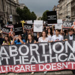 Pro-life protesters holding a sign: "Abortion Isn't Healthcare. Healthcare doesn't kill."