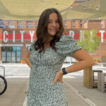 Laken Riley, a college coed, poses in front of a city market in a flower blouse.