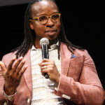 Ibram X. Kendi sits speaking into a microphone wearing a salmon blazer.