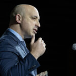 Jonathan Greenblatt in a blue suit gestures in front of a microphone