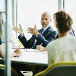 Corporate executive speaks in a suit to employees in dress clothes in a boardroom