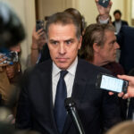 Hunter Biden stands in the middle of a crowd with microphones and cameras with a stern look on his face.