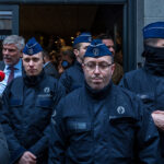 Several Brussels police officers in dark blue uniforms and caps block the entrance to a hotel