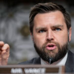 J.D. Vance gestures while wearing a suit