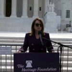 A woman speaks at a podium wearing sunglasses.