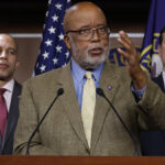 Bennie Thompson in a brown suit gestures in front of an American flag