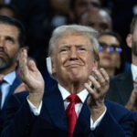 Former President Donald Trump, in a suit and clapping, pictured with his sons Don Jr. and Eric
