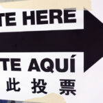 A paper sign that says "vote here" in English and Spanish
