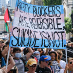 Protesters hold a sign reading, "Puberty Blockers Are Reversible, Suicide Is Not."