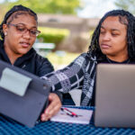 Two black female students studying together, looking at their laptops and tablets