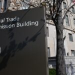 The Federal Trade Commission building stands behind a sign identifying it next to a tree.