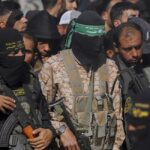 Hamas militants stand while holding machine surrounded by a crowd of people.