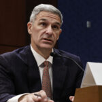 Ken Cuccinelli in a dark suit and sitting at a table testifying to a congressional committee