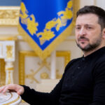 Ukrainian President Volodymyr Zelenskyy sits at a table.