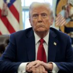 Donald Trump sits at his desk in the White House with his hands folded in front of him.