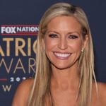 Ainsley Earthardt smiles while standing on the red carpet of an awards show.