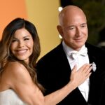 Jeff Bezos stands on a red carpet as his wife Lauren Sanchez puts her right hand on his chest.