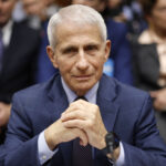 Anthony Fauci wears a blue suit as he sits with his hands clasped.