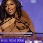 Rep. Jasmine Crockett in a light brown dress speaks at a podium in front of a purple background