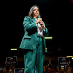 Rochelle Garza holding a microphone while standing on stage wearing a green blazer.