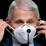 Anthony Fauci in a suit putting on an N95 mask