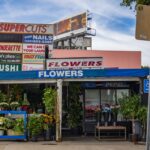 A small open-ended building has a sign that says, "Flowers" while in the background are numerous other business signs.