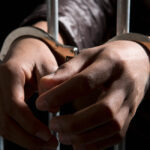 Two hands protruding from prison cell bars