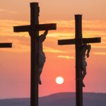 Three crosses hold men who were crucified as the sun goes down.
