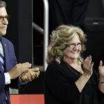 Bev Vance stands and applauds with a smile on her face as Mike Johnson stands to her right.