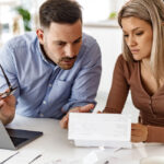 young couple sitting at the kitchen table with a laptop and tax paperwork looking worried