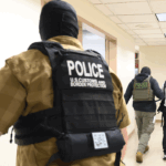 Several officers, including U.S. Customs and Border Protection, escort two individuals down a hallway in a government building.