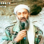 Osama Bin Laden in camouflage clothing and a white head covering speaks into a microphone against a rocky background, referencing the events of 9/11. Al-Jazeera Exclusive and Arabic text appear on the screen.