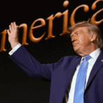Donald Trump in a dark suit and light blue tie waves with his right hand. The background shows large, partially visible golden text reading America, suggesting a Trump rally or event.