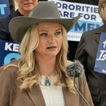 Kappa Kappa Gamma members, including Allie Coghan, sued KKG for allowing men to join the sorority. Pictured: Coghan, a woman in a cowboy hat speaks at a podium, surrounded by people holding blue signs with messages supporting women and sisterhood.