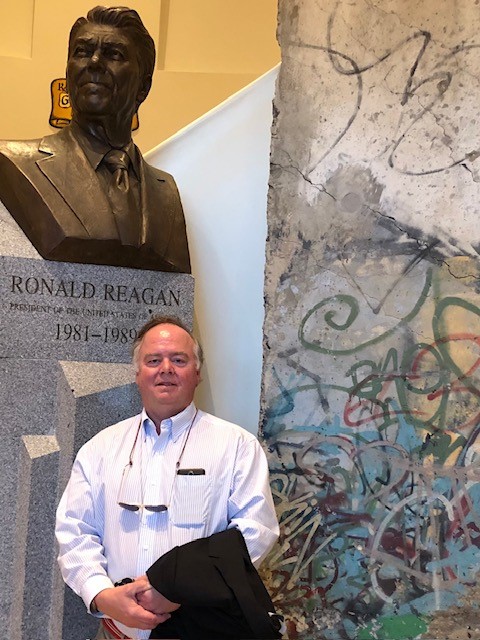 Reagan’s Berlin Wall Speech Forever Changed the World 2 A man stands next to a bust of Reagan and a graffiti-covered section of the Berlin Wall. The bust is on a pedestal labeled with Reagan’s name and term as U.S. president, 1981-1989.
