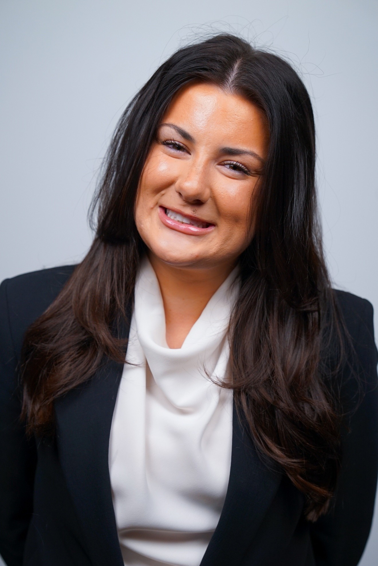 Daily Signal Internship 2 A woman with long dark hair, wearing a black blazer and white blouse, smiles at the camera against a plain light background—capturing the polished, professional look ideal for a Daily Signal internship.