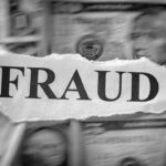 A torn piece of paper with the word FRAUD is placed over blurred U.S. dollar bills, suggesting financial deception or crime.