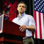Sen. Jon Ossoff stands at a podium labeled UNITED FOR GEORGIA with an American flag in the background and people watching from the side.