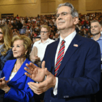 Scott Bessent Linda McMahon applaud alongside others in a crowded auditorium at a Donald Trump campaign event.