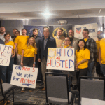 A large group of people smiles and poses for a photo holding signs supporting Jon Husted, including messages that say Husted for Ohio, On Nov 3rd We vote for Husted, and Ohio 4 Husted.