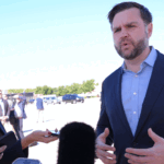 J.D. Vance speaking to reporters holding microphones and a camera.
