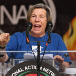 American Federation of Teachers (AFT) President Randi Weingarten, a woman speaking at a podium with two microphones, with the National Action Network logo and a flame graphic in the background.