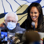 Melat Kiros, a DSA candidate, smiles with a cardboard cutout of Bernie Sanders wearing a mask.