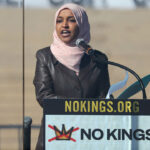 Ilhan Omar in a pink headscarf speaks at a NOKINGS.ORG podium, highlighting immigrants’ voices, with NO KINGS and a crossed-out crown graphic. Steps are visible in the background.