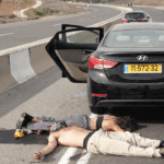 Two people lie motionless on the asphalt next to a black sedan with its rear door open on the shoulder of a highway after Oct. 7 attacks.