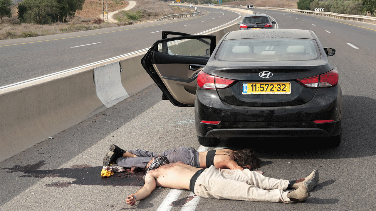 Home 2 Two people lie motionless on the asphalt next to a black sedan with its rear door open on the shoulder of a highway after Oct. 7 attacks.
