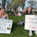 Two people sitting on a Charlottesville lawn hold protest signs that read No freedom til were equal and You cant control me fascist.