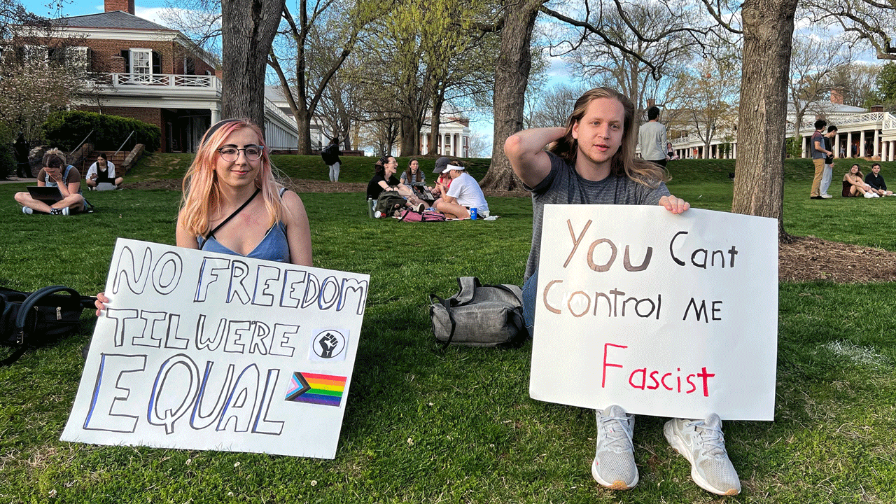 Two people sitting on a Charlottesville lawn hold protest signs that read No freedom til were equal and You cant control me fascist.
