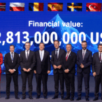 A group of NATO officials standing in a line in front of a digital screen displaying a financial value of 2,813,000,000 USD and various national flags.